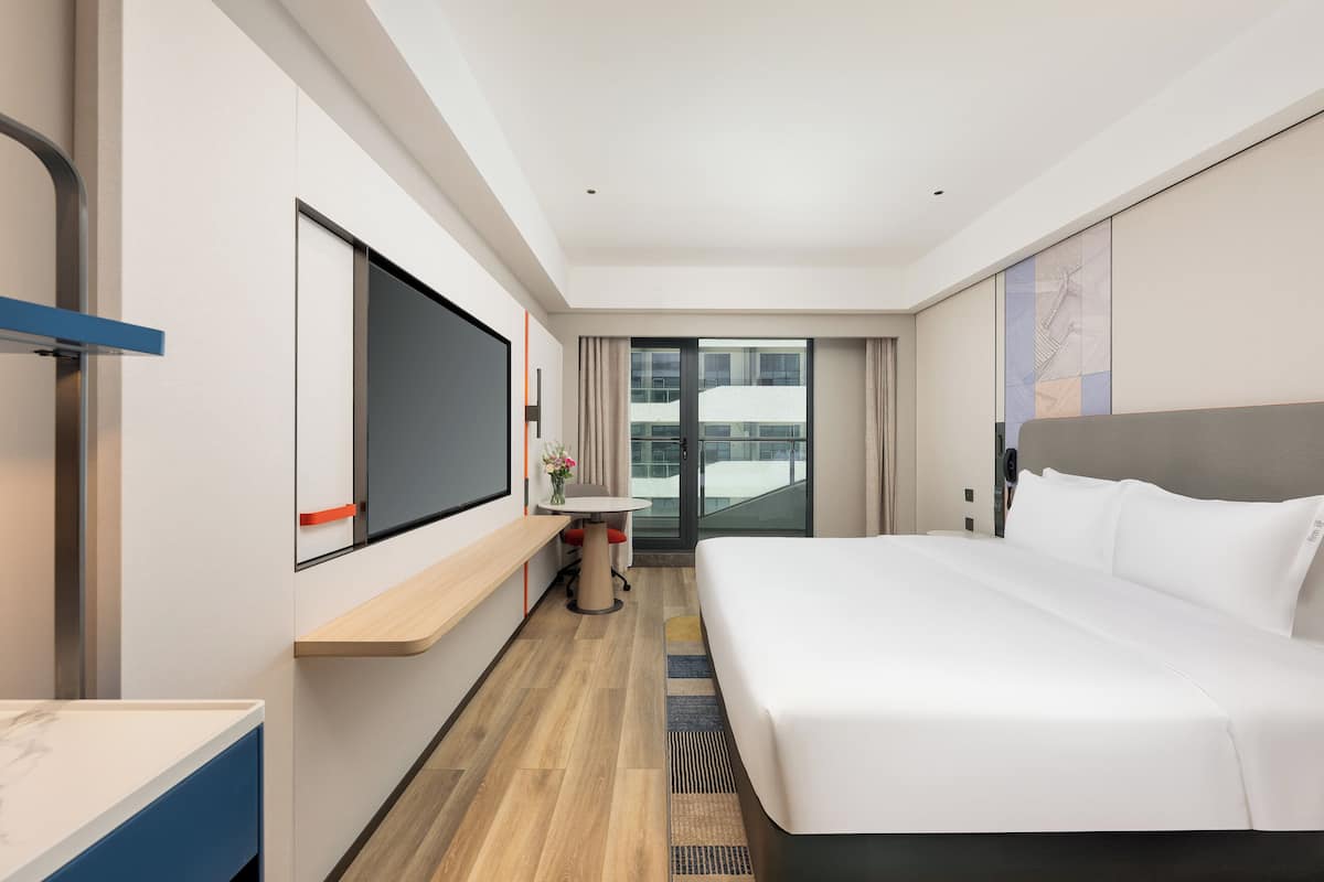 A modern hotel room with a large bed, a desk, and a large window.