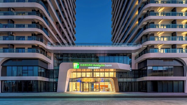 Un hôtel moderne à la façade incurvée, doté de nombreux balcons et d’une entrée imposante avec des portes en verre.