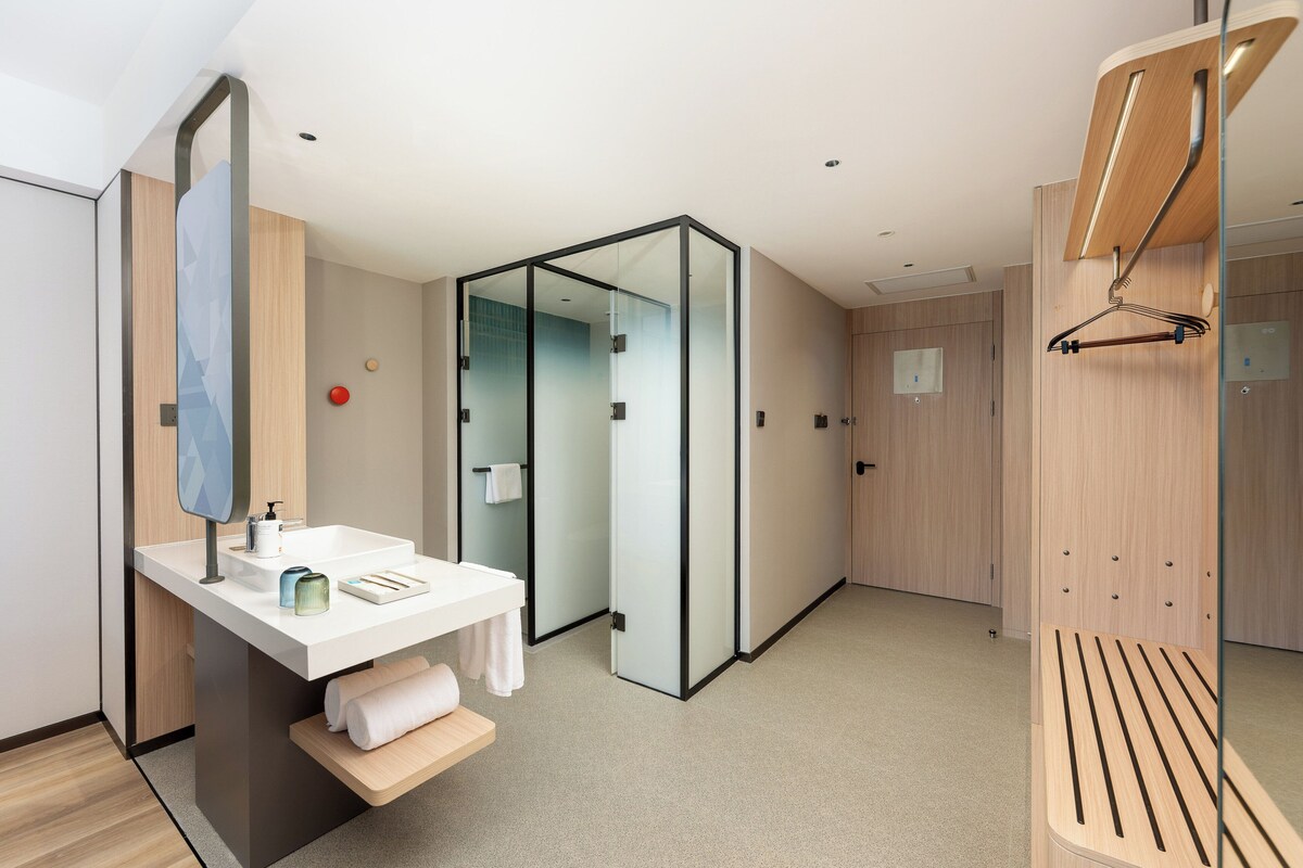 A modern bathroom with a glass partition, a white sink, and a wooden bench.