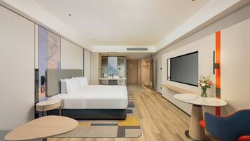 A modern hotel room with a large bed, a TV, a desk, and a chair.