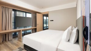 Ein modernes Hotelzimmer mit einem großen Bett, einem Flachbildfernseher, einer hölzernen Sitzbank und einem großen Fenster mit Blick auf die Stadt.