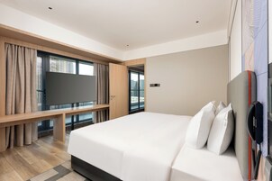 Habitación de hotel moderna con una cama grande, un televisor de pantalla plana, un banco de madera y un amplio ventanal con vistas a la ciudad.