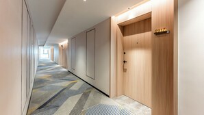 Un couloir d’hôtel avec un tapis à motifs, des portes en bois et un panneau indiquant le numéro de la chambre.