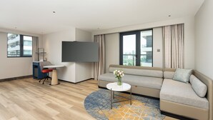 Un salon moderne comprenant un canapé, une petite table ronde, un téléviseur et un bureau avec une chaise.