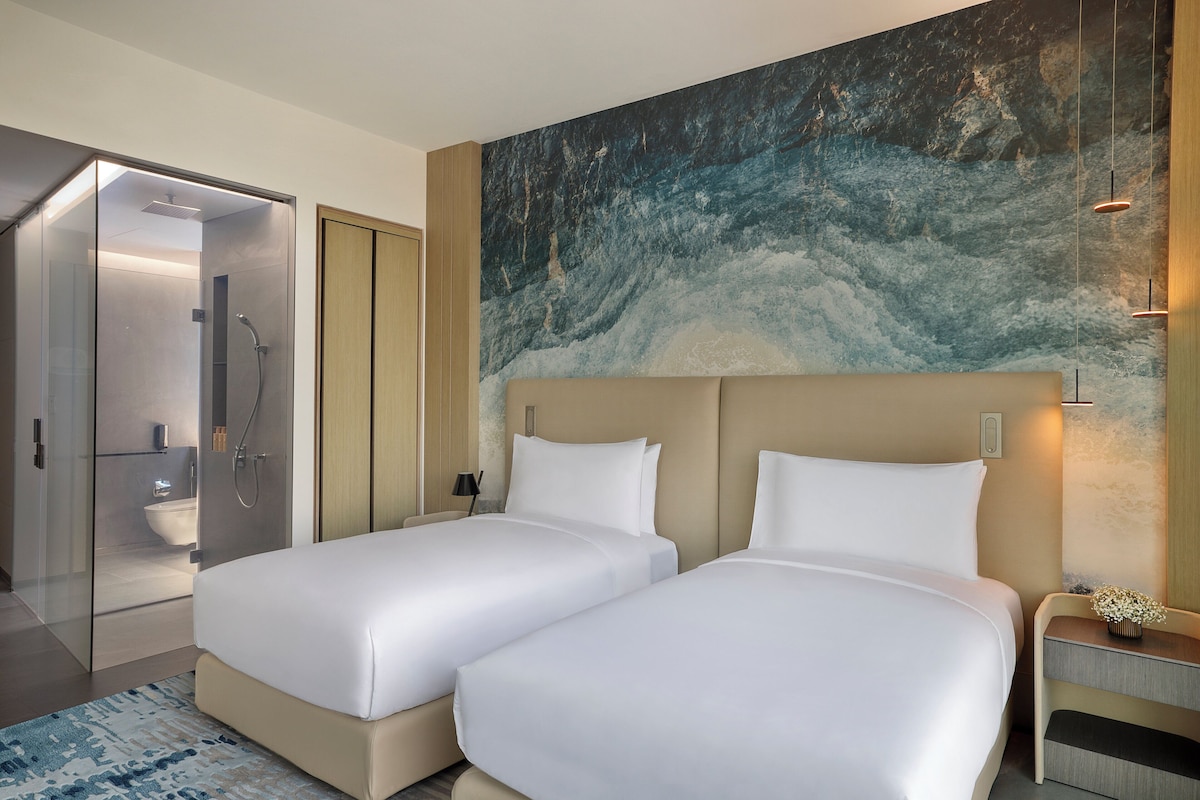 Ein Hotelzimmer mit zwei Betten, einer Duschkabine und einem großen, abstrakten Gemälde an der Wand.