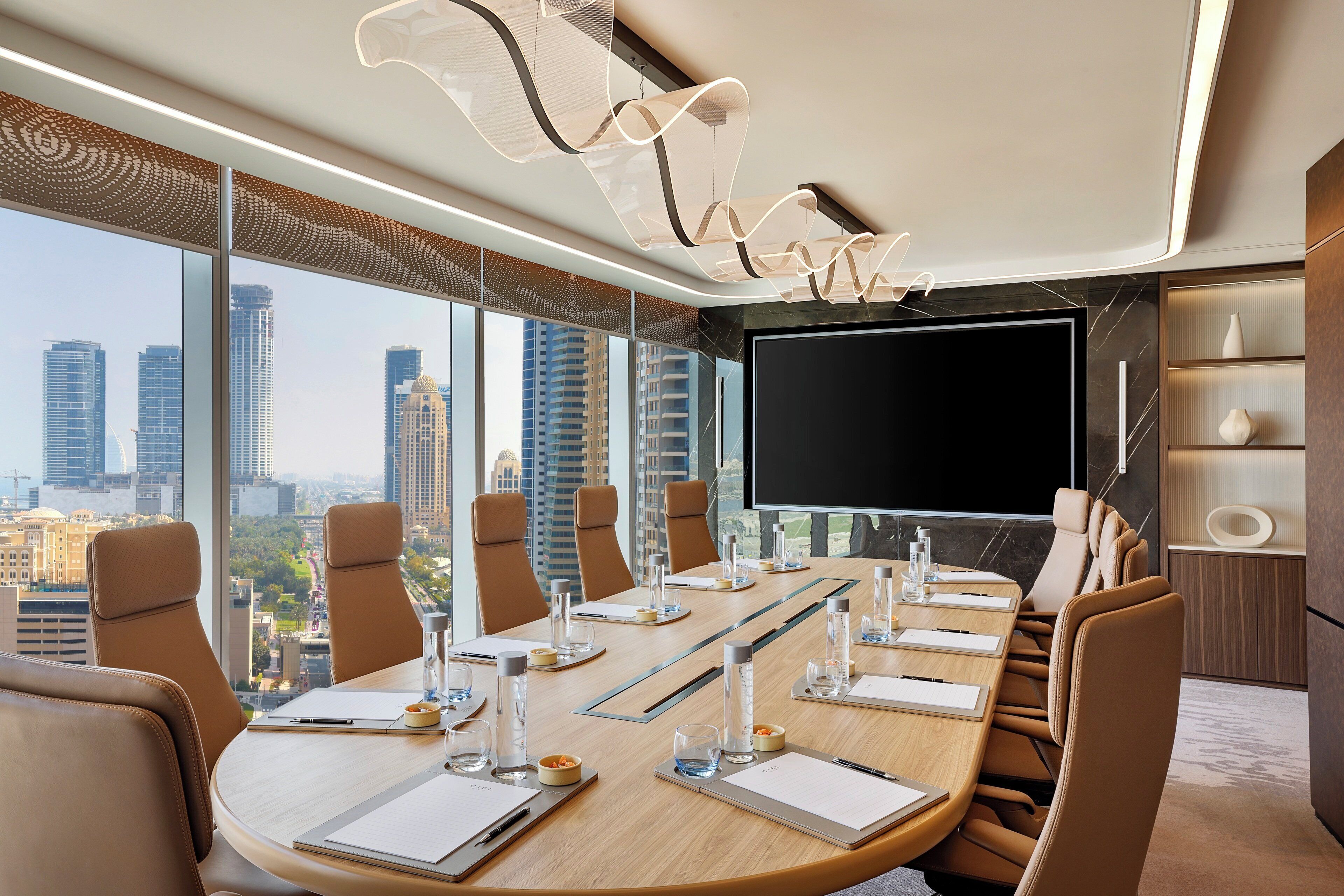 A conference room with a large table, chairs, a flat-screen TV, and a city view.