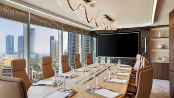 A conference room with a large table, chairs, a flat-screen TV, and a city view.
