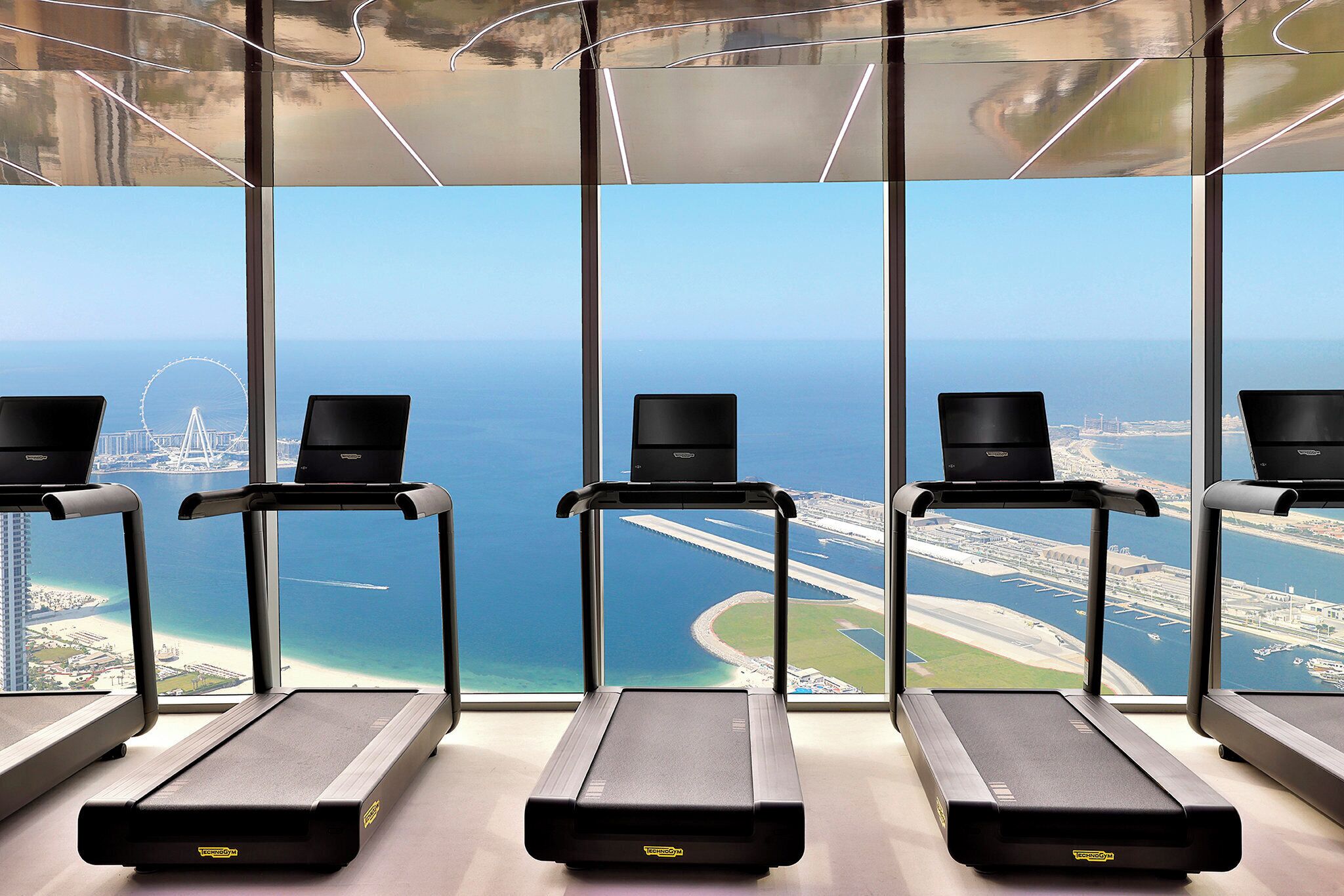 A gym with treadmills and a large window offering a view of the sea and a bridge.