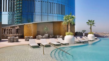 A rooftop pool area with lounge chairs, a bar, and a view of a modern building.