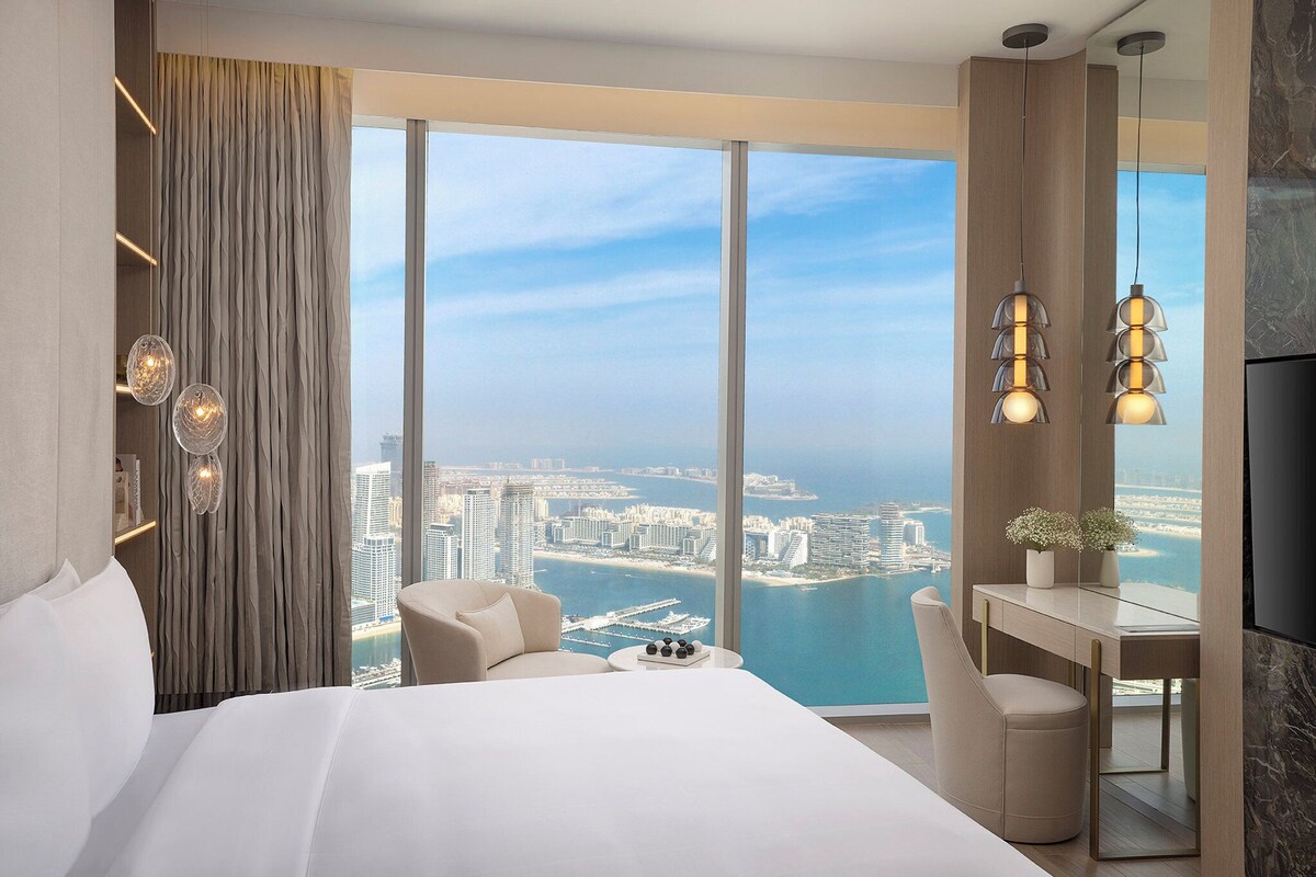 A modern hotel room with a large bed, a desk, and a view of the city and water.
