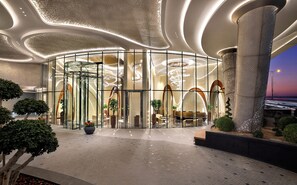 Um hall de hotel moderno com entrada em vidro curvo, área de estar central e teto decorativo.