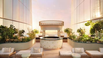 A modern rooftop lounge with a central circular seating area, surrounded by lounge chairs and planters.