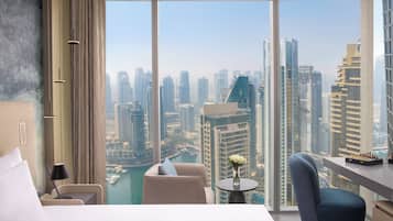 A modern hotel room with a large window offering a city view, a bed, a desk, and a chair.