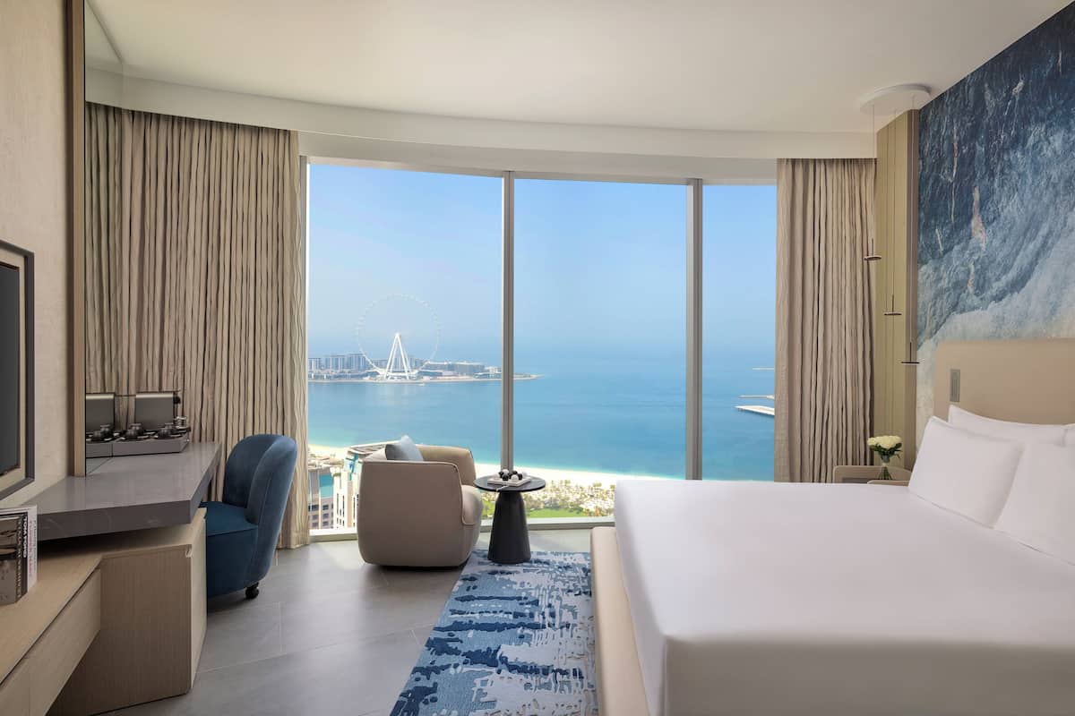A hotel room with a large window, a bed, a desk with a TV, and a chair.