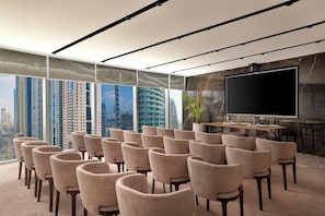 Un salón de conferencias con una pantalla grande, varias sillas y vistas a la ciudad.