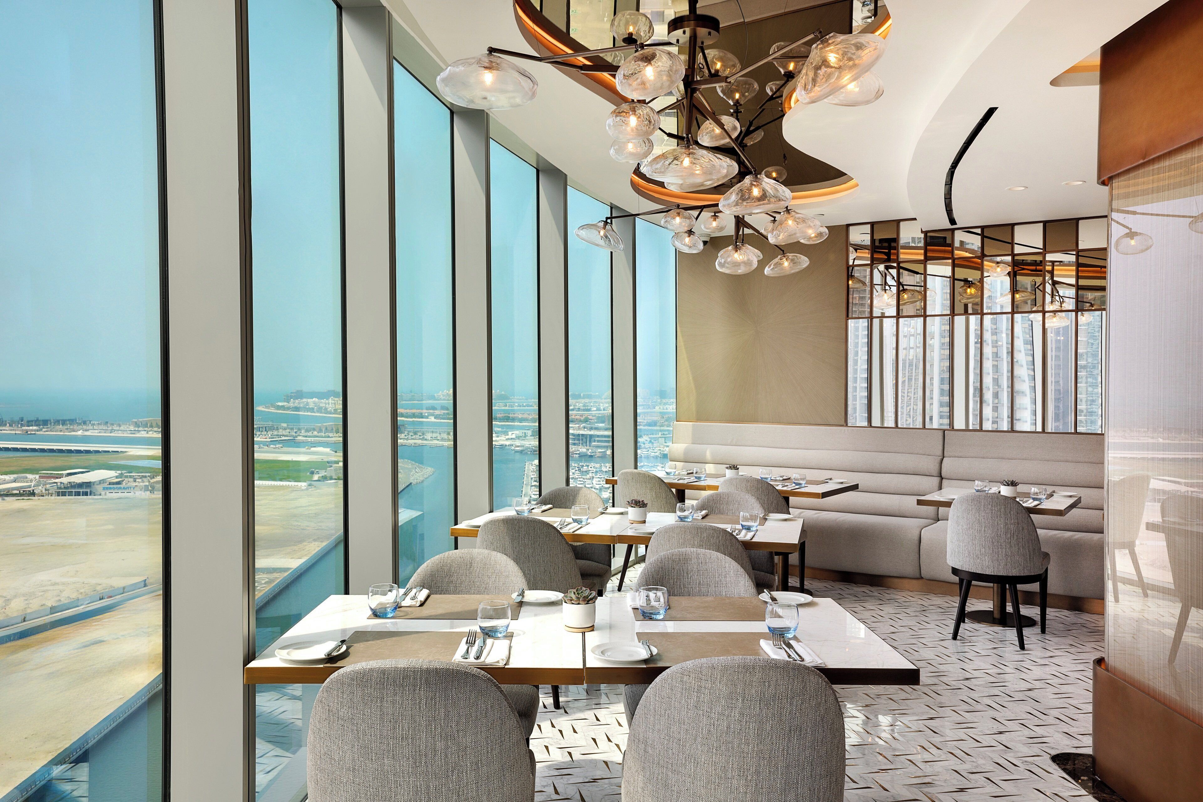 A modern dining area with high ceilings, large windows, and a view of the cityscape.