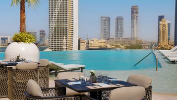 A poolside area with wicker furniture, a table set for dining, and a cityscape view in the background.
