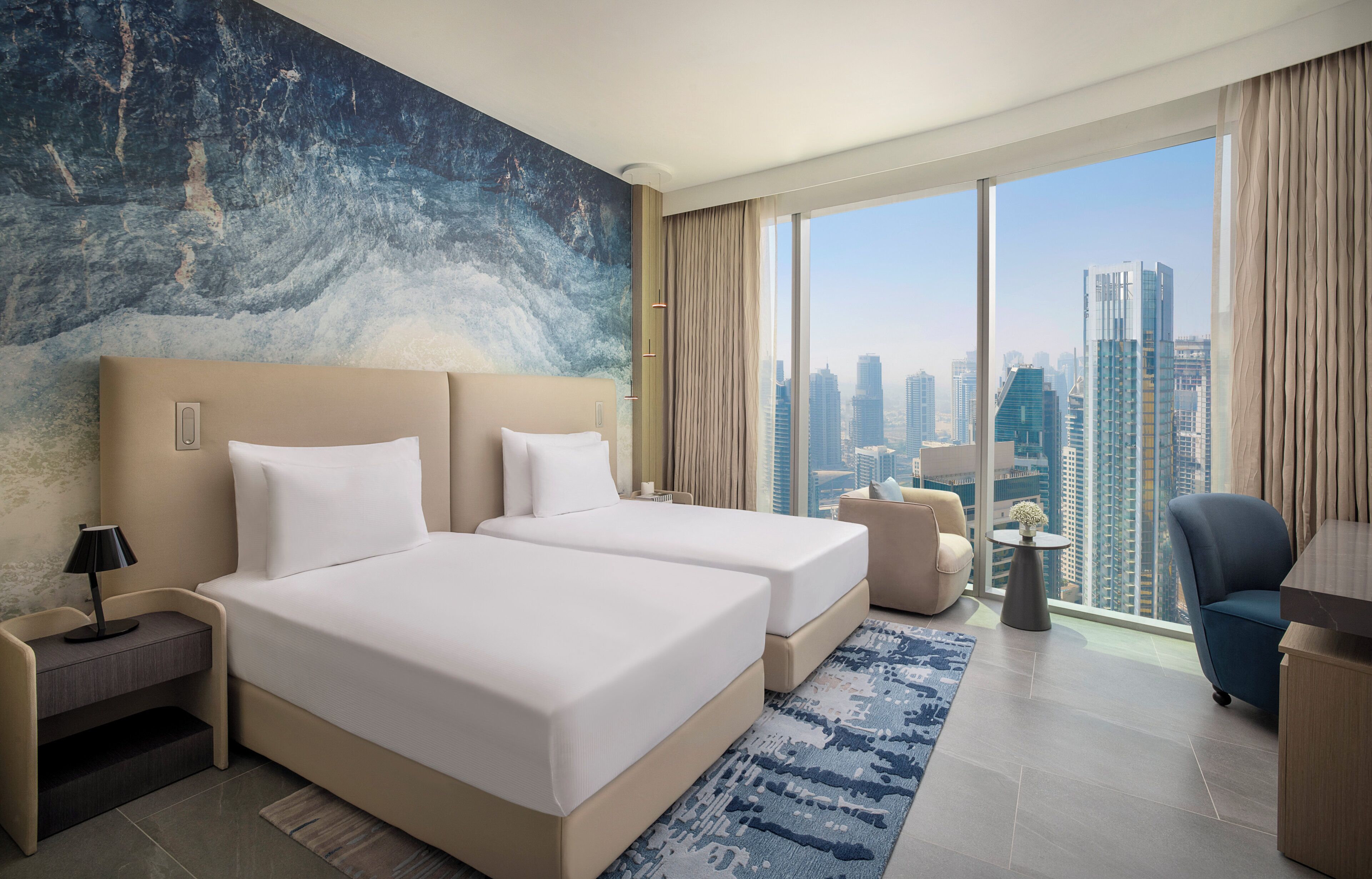 Camera d'hotel con un letto grande, una scrivania, una sedia, un tavolino e vista sullo skyline della città.