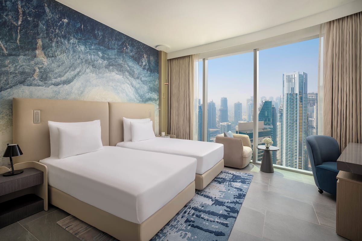 A hotel room with a large bed, a desk, a chair, a small table, and a view of the city skyline.
