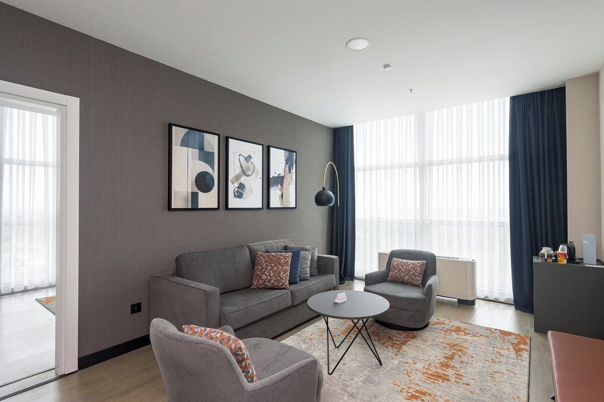 Una sala de estar moderna con un sofá gris, dos sillones, una mesa de centro y obras de arte en la pared.