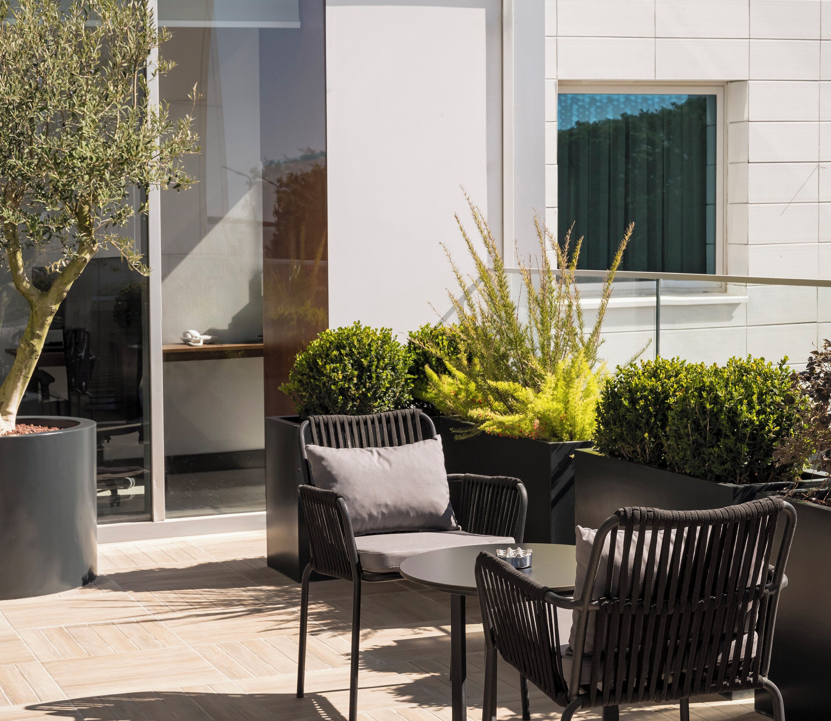 An outdoor patio with a table and chairs, a potted plant, and a modern building in the background.