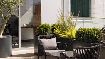 An outdoor patio with a table and chairs, a potted plant, and a modern building in the background.