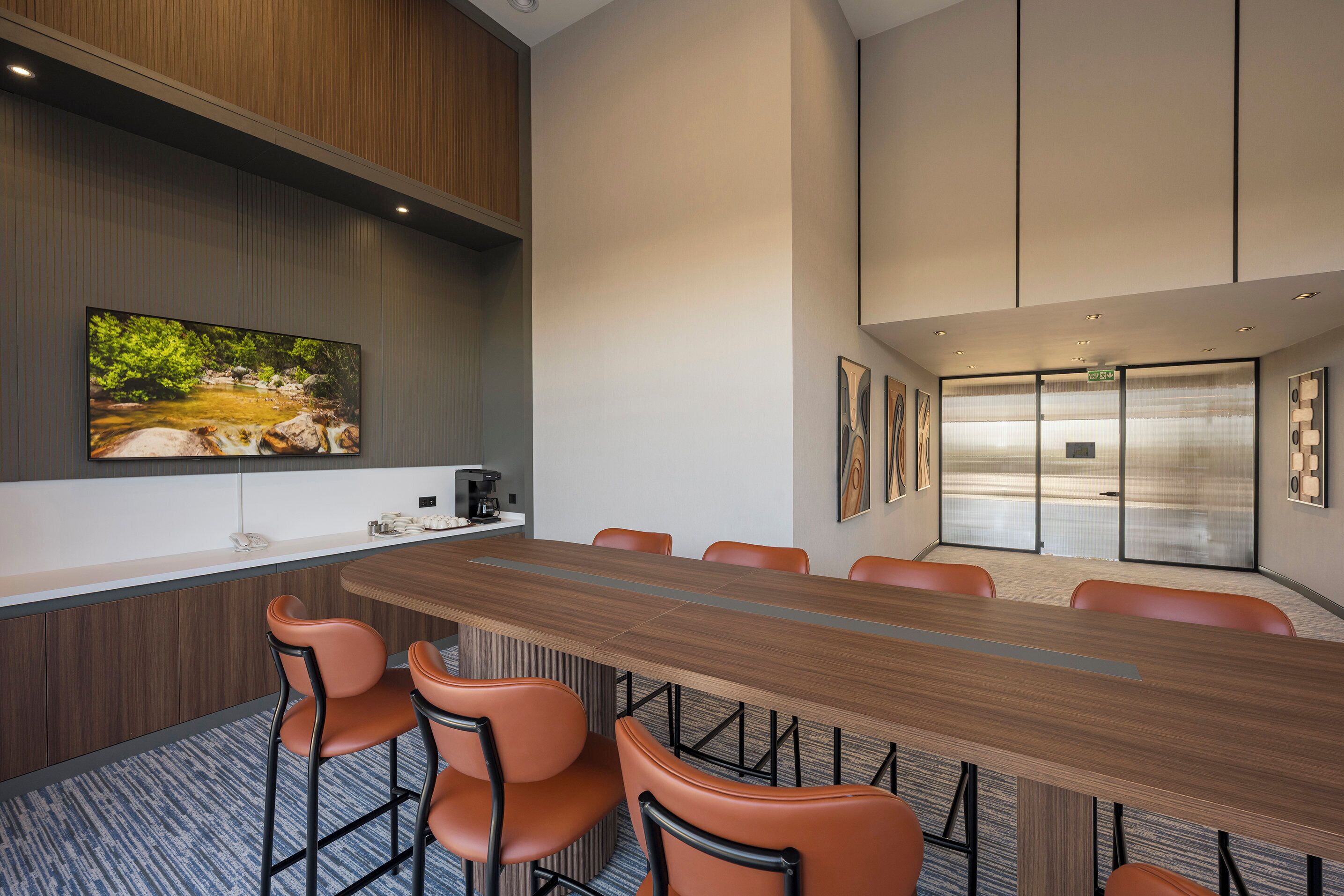 Une salle de conférence avec une longue table, des chaises orange, un coin café et un grand tableau accroché au mur.
