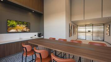 Une salle de conférence avec une longue table, des chaises orange, un coin café et un grand tableau accroché au mur.