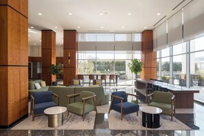 Un vestíbulo espacioso con diseño moderno, que incluye una zona de estar con sofás y sillones, un bar y grandes ventanales con vistas al exterior.