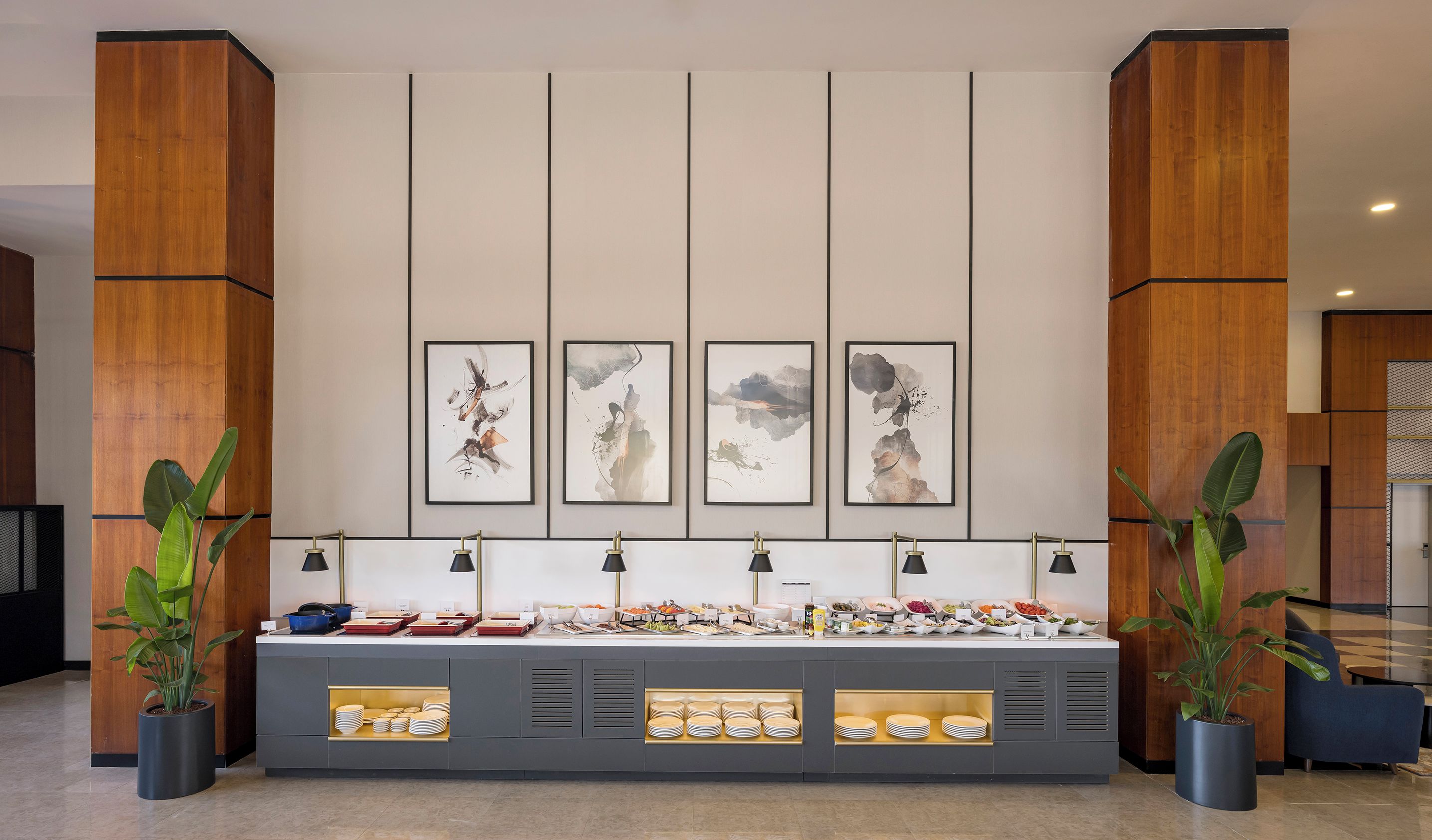 Een buffetgedeelte met diverse gerechten, een muur met abstracte kunst en potplanten.