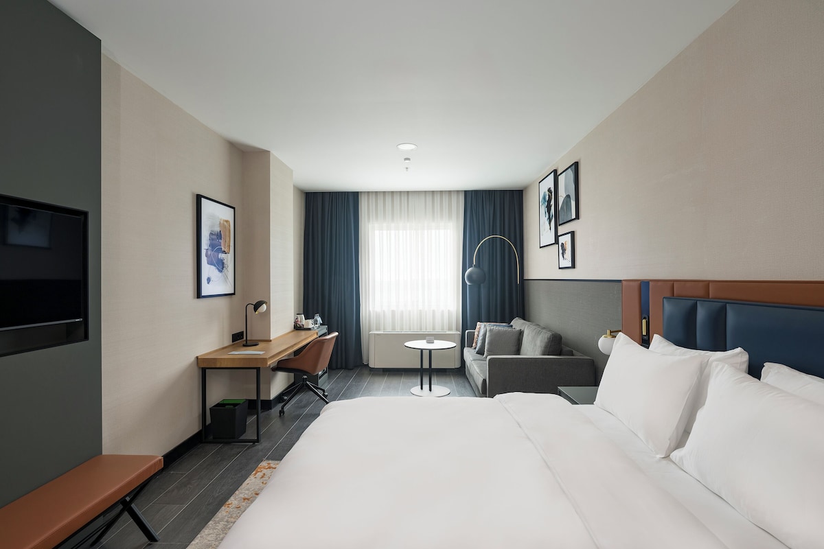 Une chambre d’hôtel avec un grand lit, un bureau avec une chaise, un canapé, une petite table et un téléviseur fixé au mur.