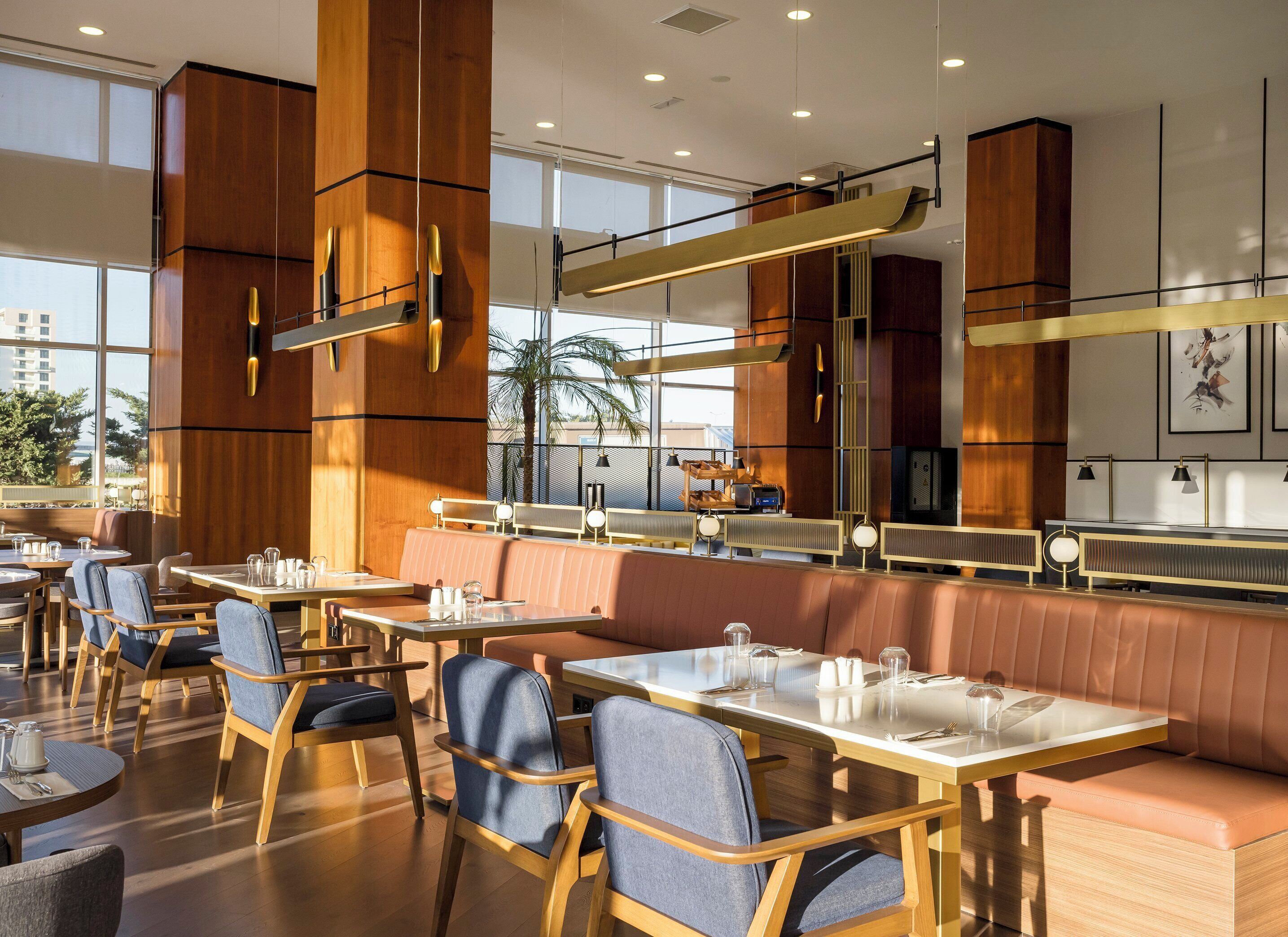 A modern restaurant interior with wooden paneling, glass tables, and cushioned seating.
