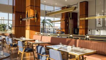 A modern restaurant interior with wooden paneling, glass tables, and cushioned seating.