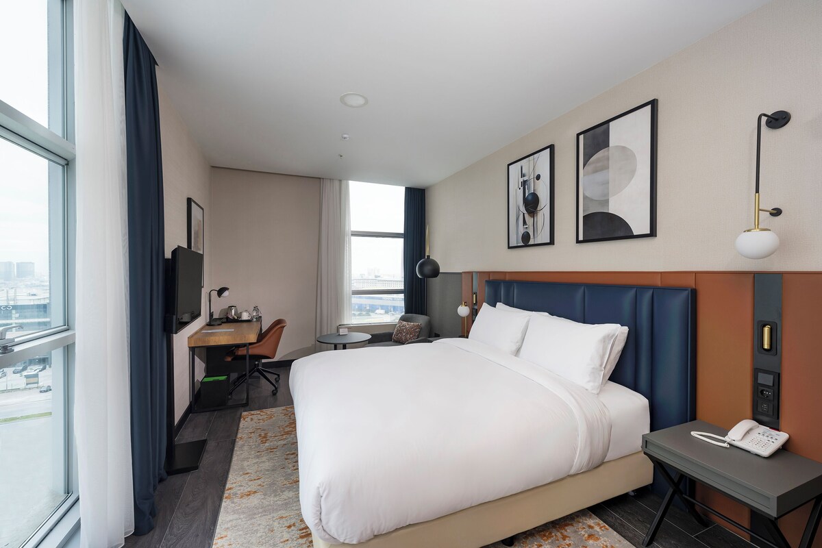 Habitación de hotel con una cama grande, un escritorio, una silla, una mesita, un teléfono y obras de arte en la pared.
