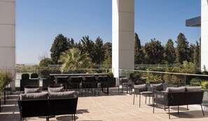 Eine Terrassengruppe im Freien mit Korbmöbeln, einer Glasumlaufung und Blick auf Bäume und Hügel.