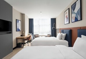 Habitación de hotel con dos camas, un escritorio, un televisor y obras de arte en las paredes.