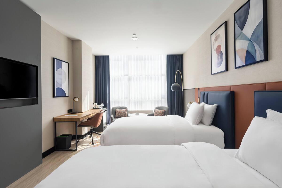 Une chambre d’hôtel avec deux lits, un bureau, une télévision et des œuvres d’art accrochées aux murs.
