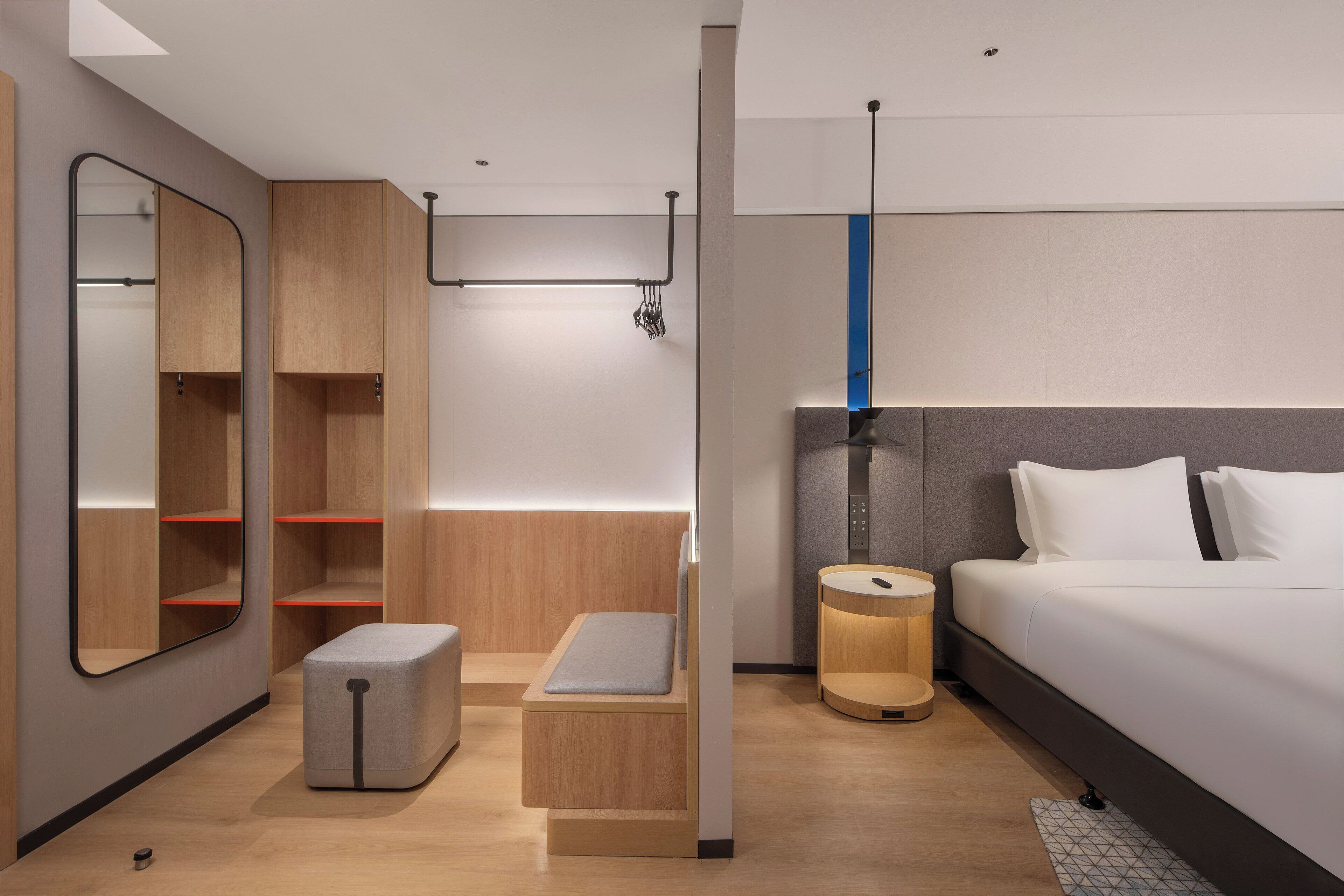 A modern hotel room with a bed, bedside table, nightstand, and built-in wardrobe.