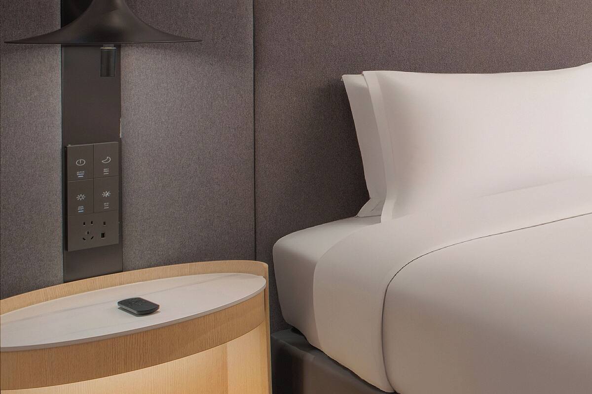 Ein modernes Hotelzimmer mit Bett, Nachttisch mit Lampe und Bedienfeld.