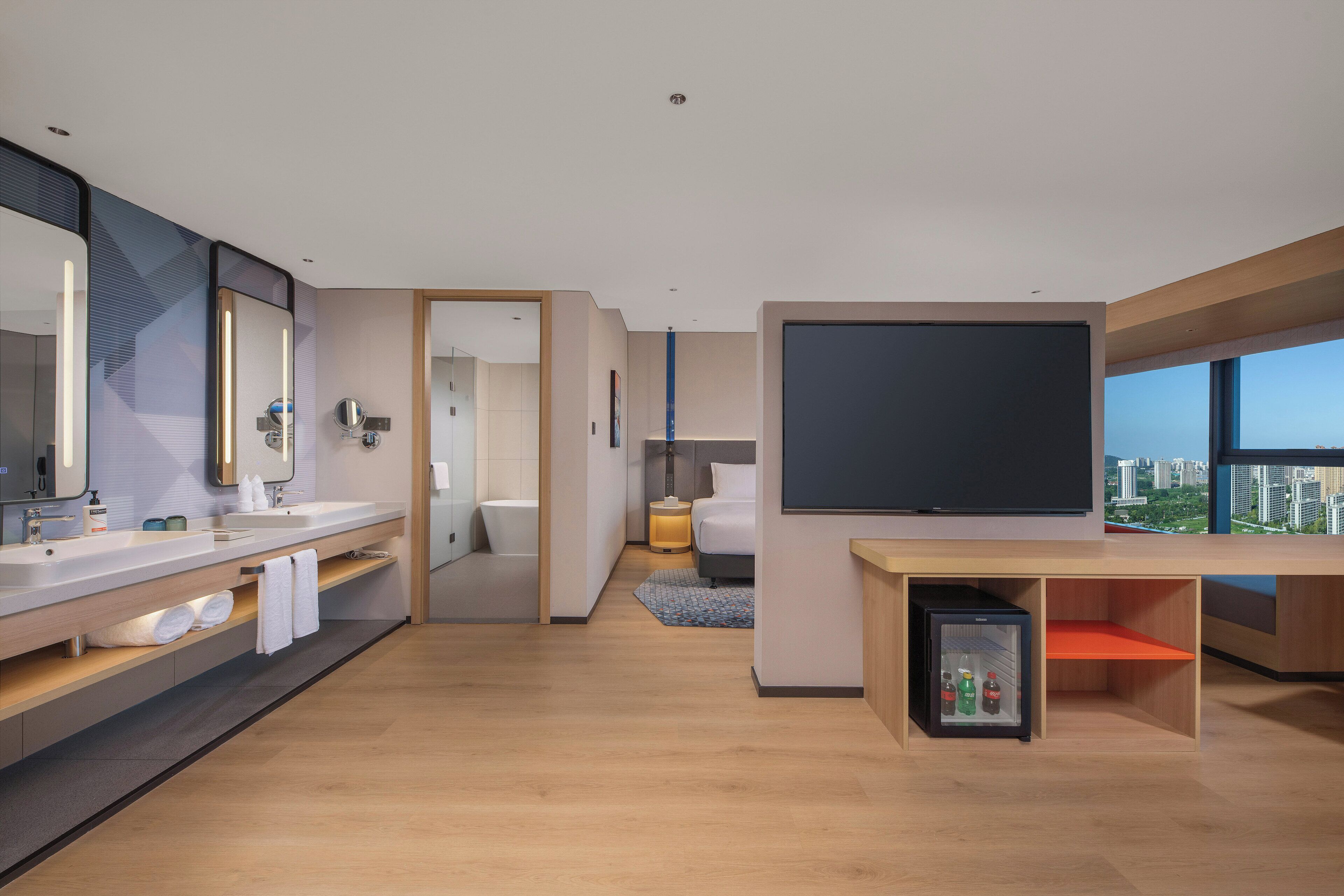 Una habitación de hotel moderna con un televisor grande, un minibar y vistas a la ciudad.