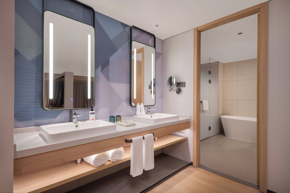 A modern bathroom with two sinks, a large mirror, and a bathtub.