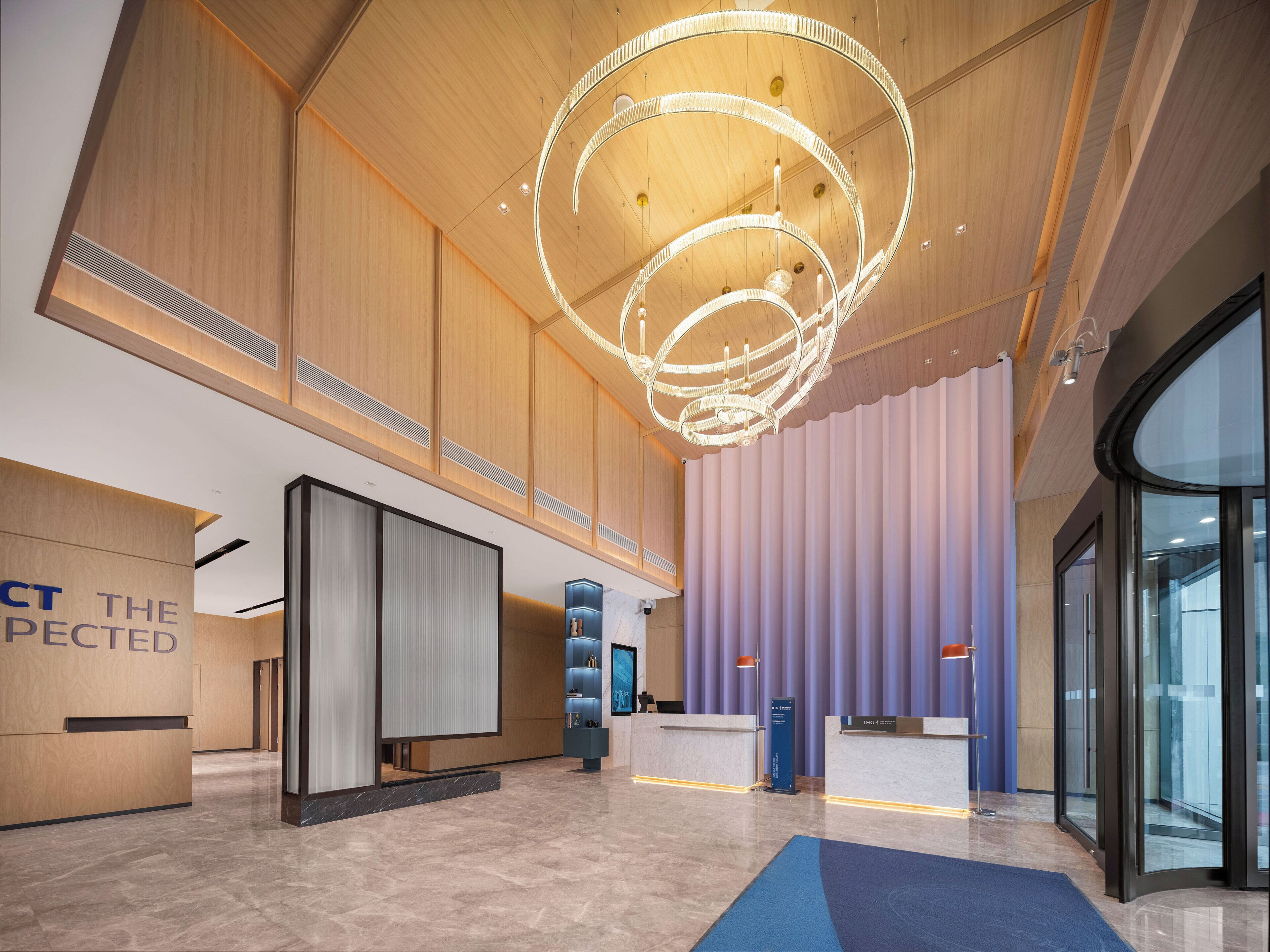 A modern hotel lobby with a wooden ceiling, a circular light fixture, and a reception desk.
