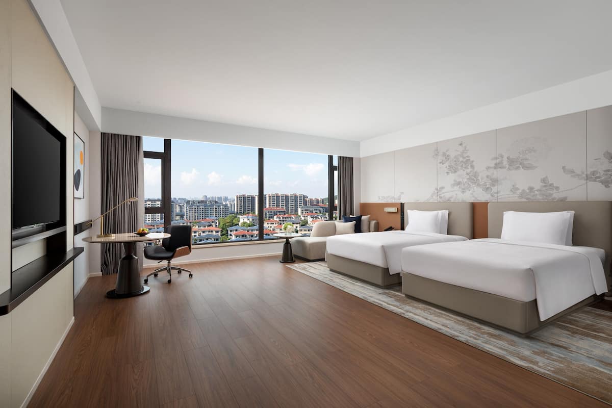 Une chambre d’hôtel avec une grande fenêtre, un lit, un bureau et une chaise.