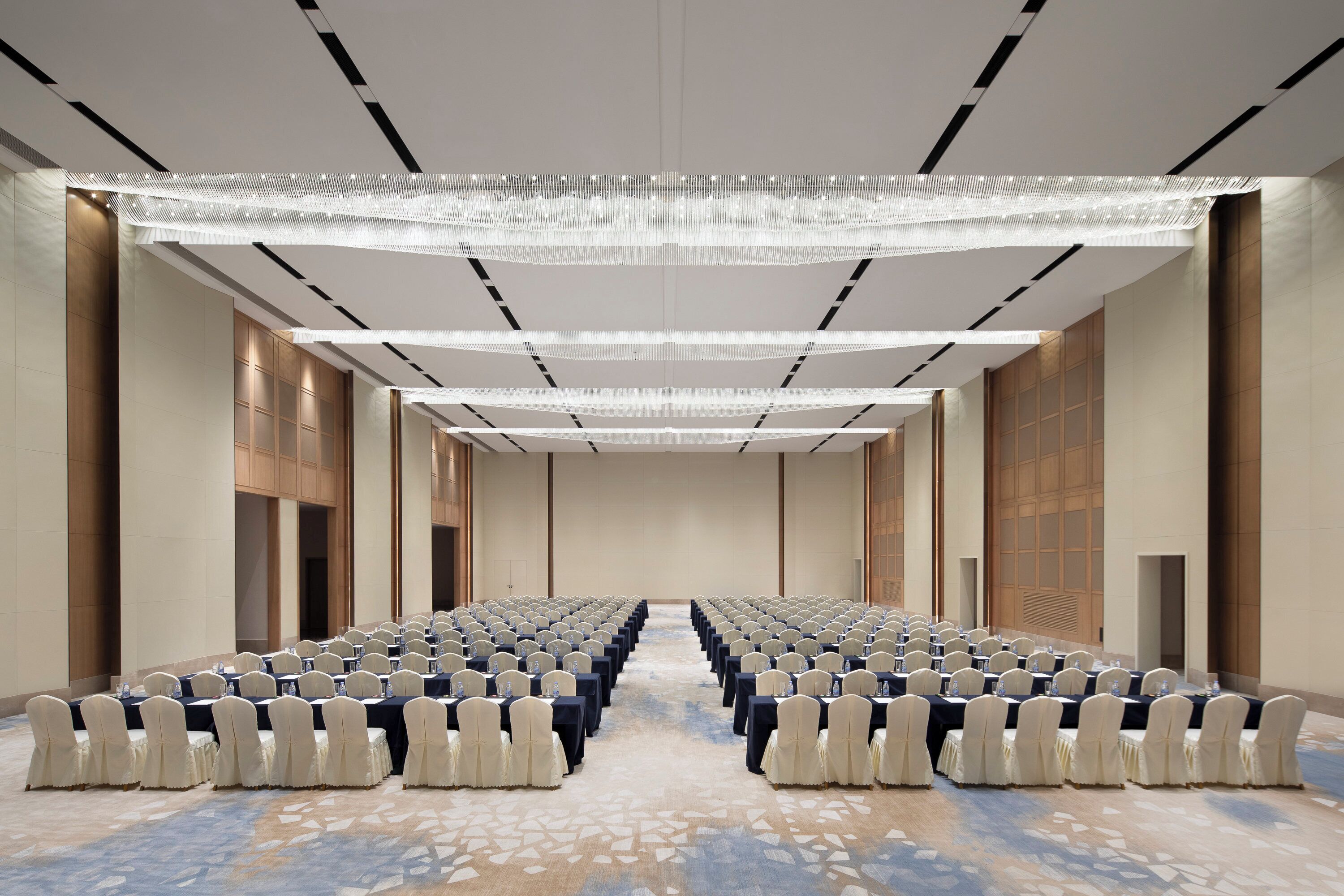 A conference room with rows of tables and chairs, a patterned carpet, and a modern ceiling design.