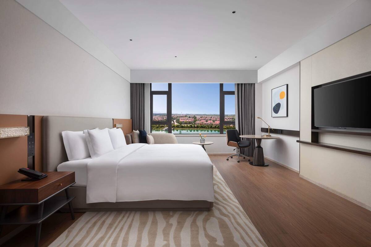 Une chambre d’hôtel moderne dotée d’un grand lit, d’un bureau, d’une chaise, d’une télévision et offrant une vue sur le paysage urbain.