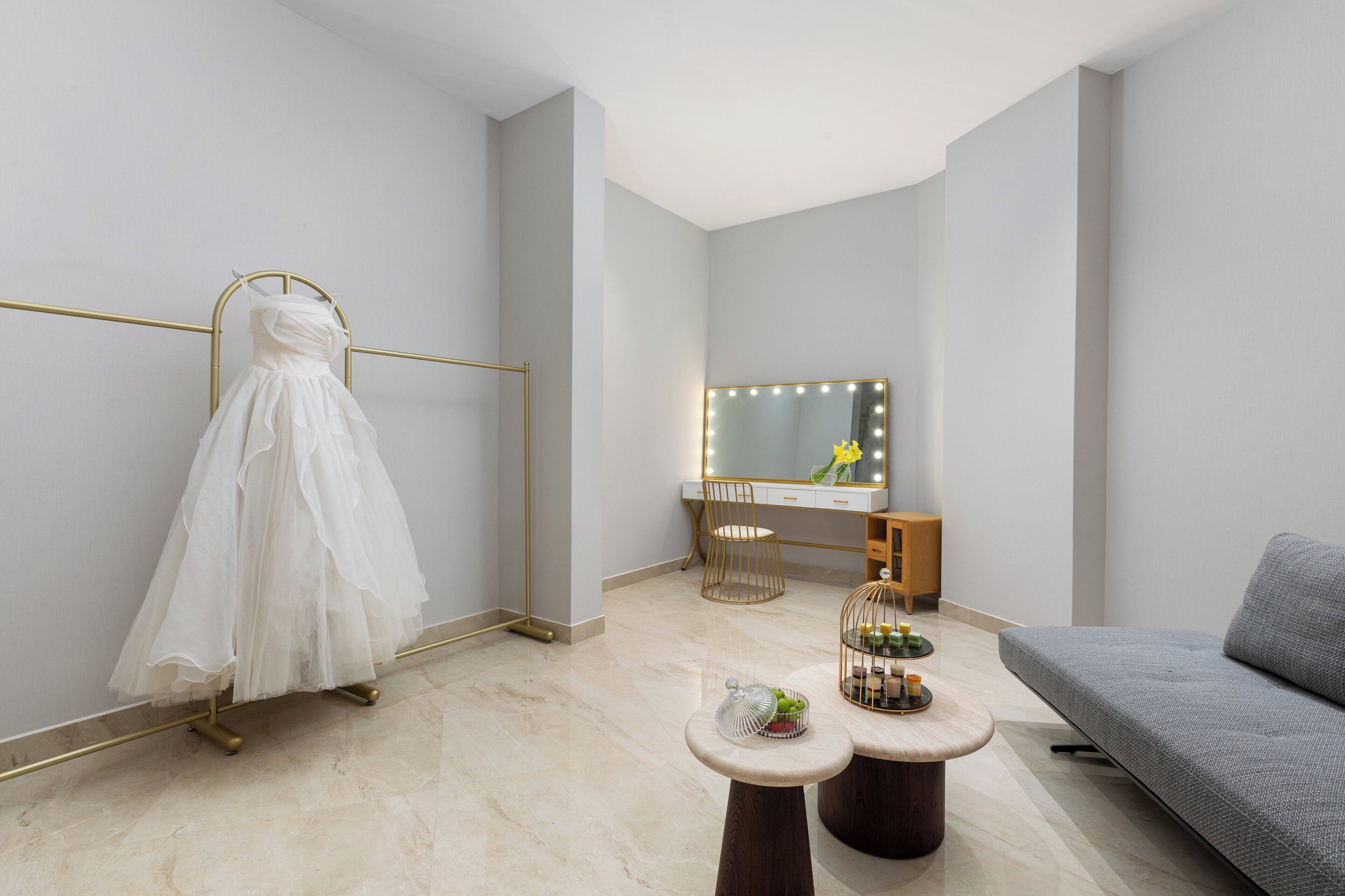 A room with a dress on a stand, a vanity with a mirror, and a sofa.
