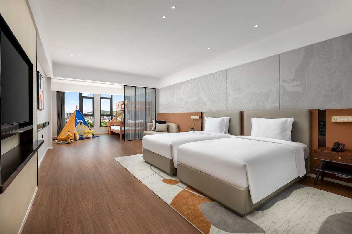 Une chambre d’hôtel moderne équipée de deux lits, d’un téléviseur à écran plat, d’un bureau avec un téléphone et offrant une vue sur le paysage urbain.