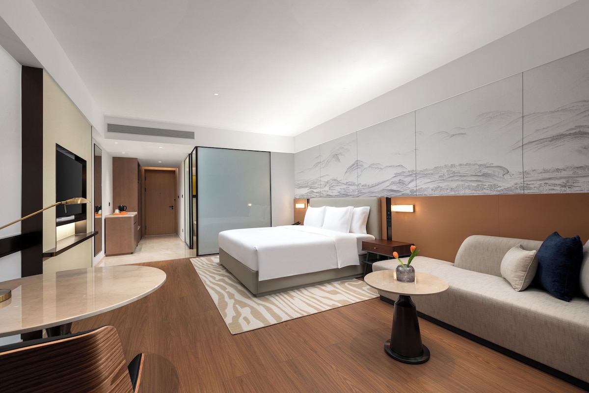 Une chambre d’hôtel moderne équipée d’un lit, d’un canapé, d’une télévision et d’un mur décoré d’œuvres d’art.
