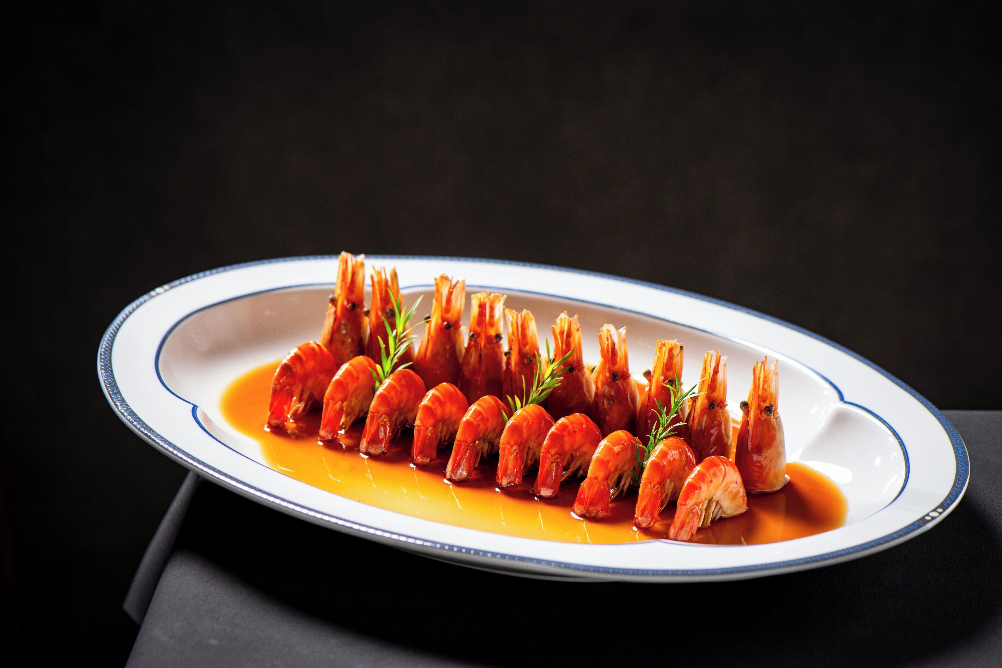 A plate of cooked shrimp arranged in a row on a white plate with a blue rim.