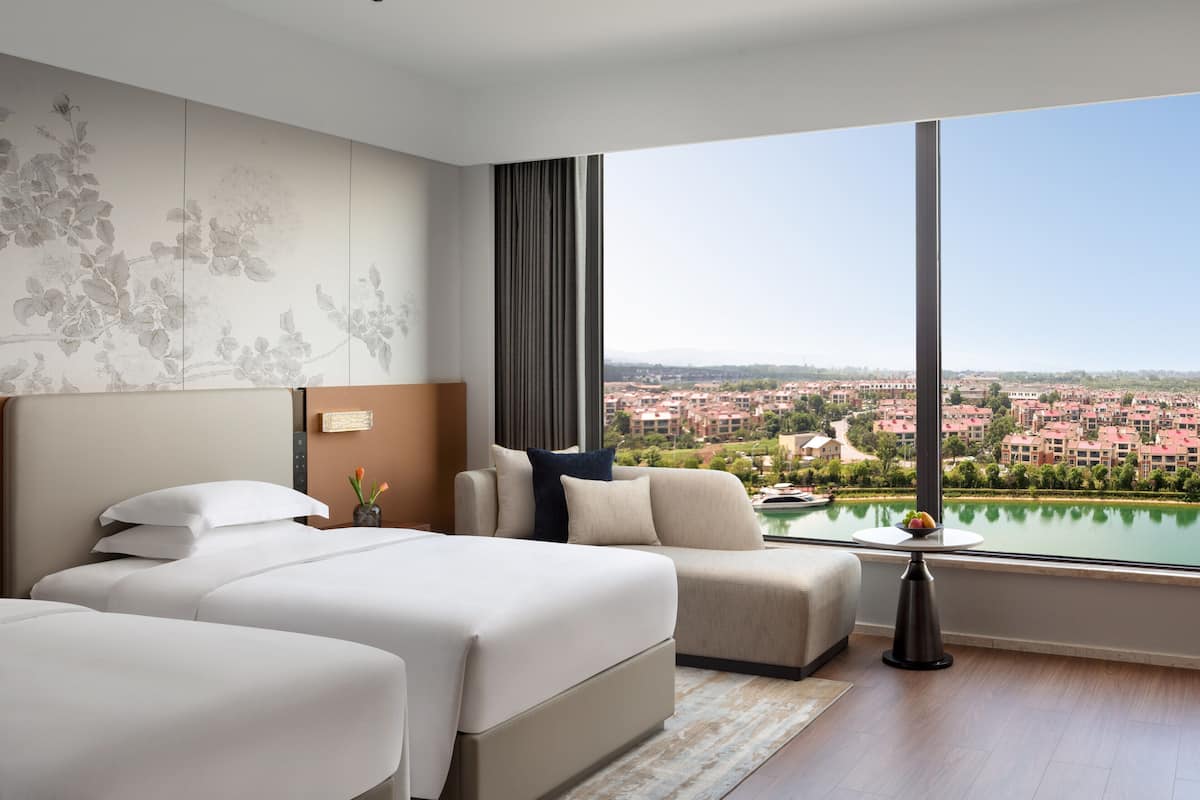 Une chambre d’hôtel avec un grand lit, un canapé, une vue sur la ville et un balcon donnant sur un plan d’eau.